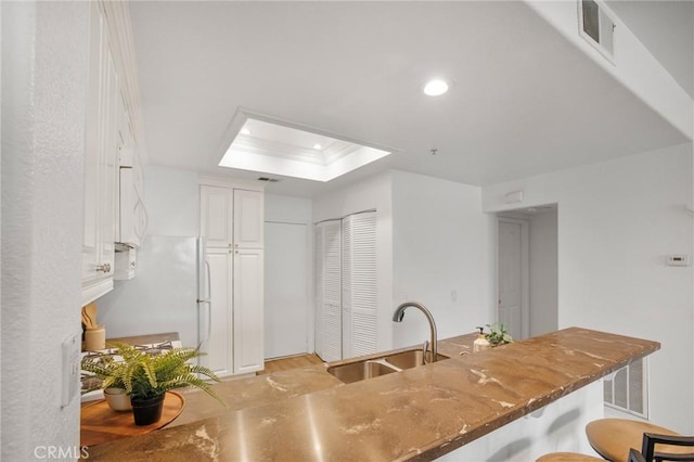 kitchen with visible vents, a breakfast bar area, dark stone countertops, a skylight, and a sink