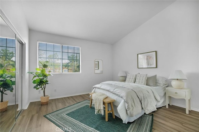 bedroom featuring access to exterior, lofted ceiling, wood finished floors, and baseboards