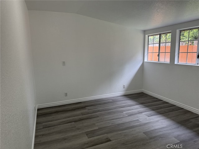 unfurnished room featuring dark wood-type flooring, lofted ceiling, a textured ceiling, baseboards, and a textured wall