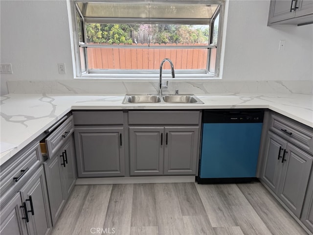 kitchen featuring dishwashing machine, light stone counters, gray cabinets, a sink, and light wood-type flooring