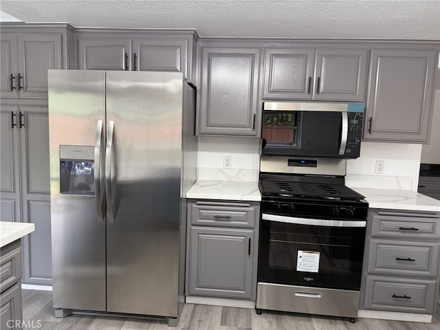 kitchen featuring light wood-style floors, appliances with stainless steel finishes, gray cabinets, and a textured ceiling