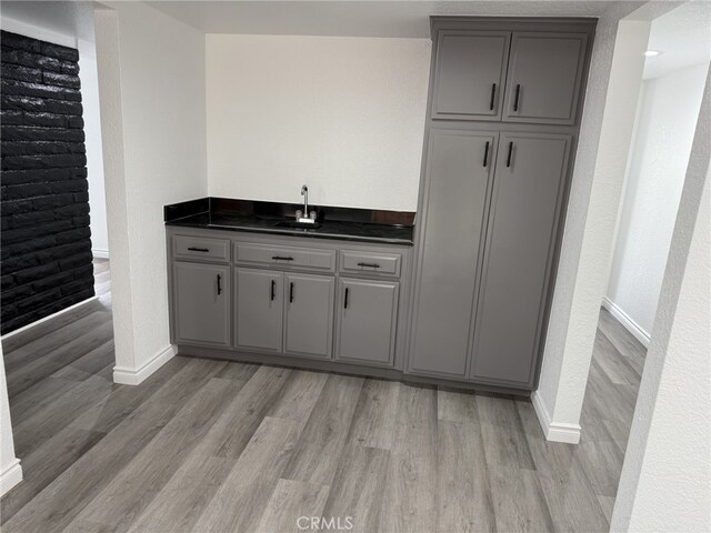 bar featuring indoor wet bar, light wood-style flooring, baseboards, and a sink