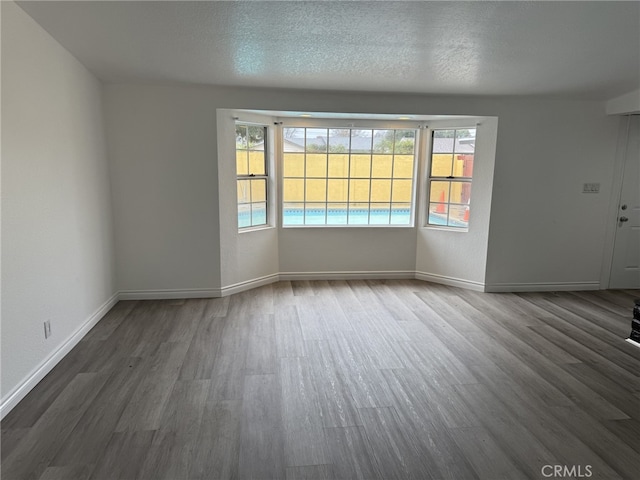 unfurnished room featuring plenty of natural light, a textured ceiling, baseboards, and wood finished floors