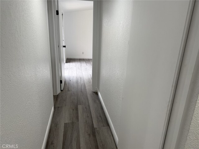 corridor featuring wood finished floors, a textured wall, and baseboards