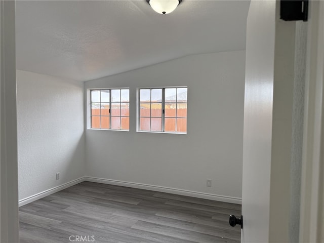 unfurnished room with baseboards, lofted ceiling, a textured ceiling, and wood finished floors