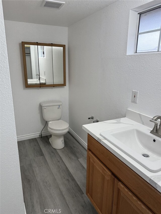 bathroom featuring visible vents, baseboards, toilet, wood finished floors, and vanity