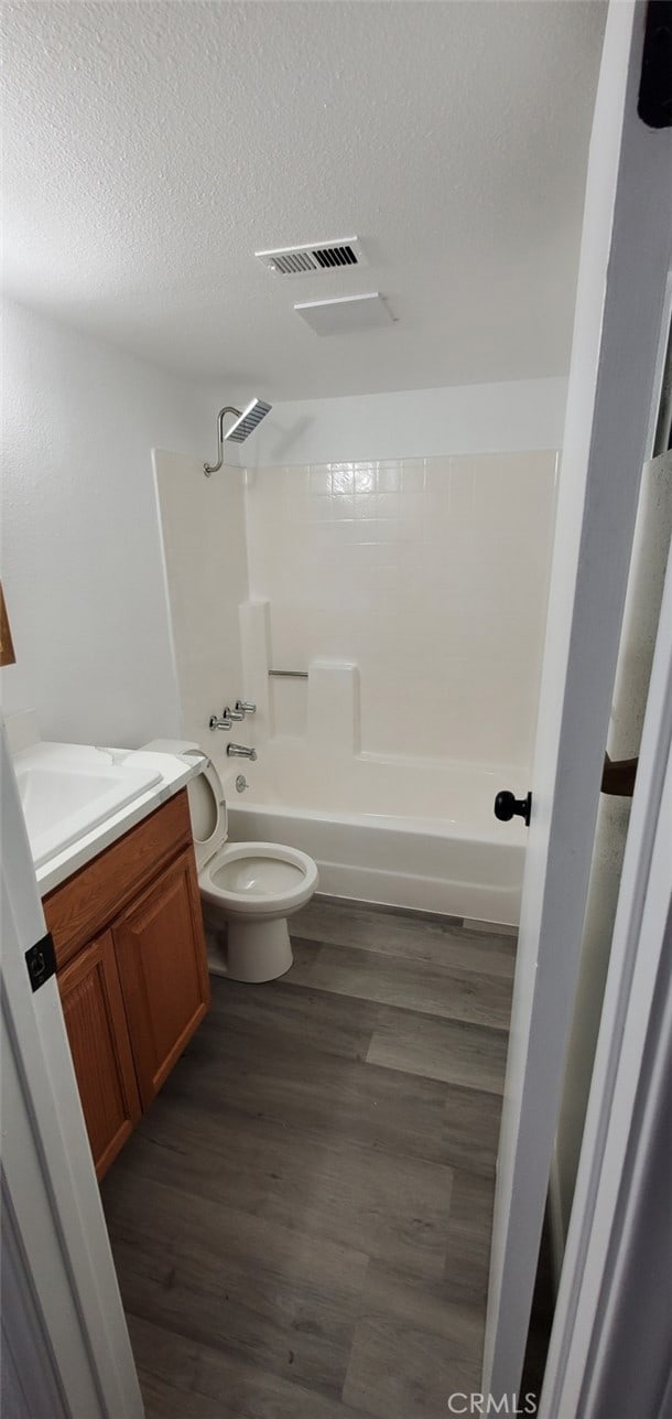 full bathroom with wood finished floors, visible vents, tub / shower combination, a textured ceiling, and toilet