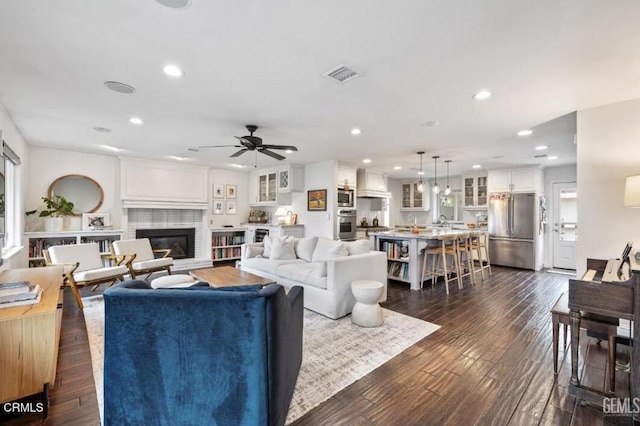 living room with visible vents, a glass covered fireplace, dark wood-style floors, recessed lighting, and ceiling fan