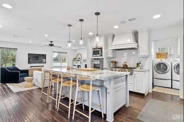 kitchen featuring premium range hood, dark wood-style floors, washing machine and dryer, stainless steel appliances, and white cabinets