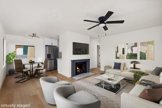 living room with a fireplace, light wood finished floors, and ceiling fan