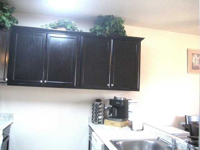 kitchen featuring dishwasher, dark cabinetry, light countertops, and a sink