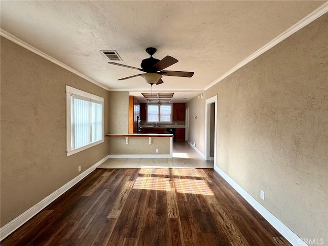 unfurnished living room featuring visible vents, ornamental molding, wood finished floors, baseboards, and a textured wall