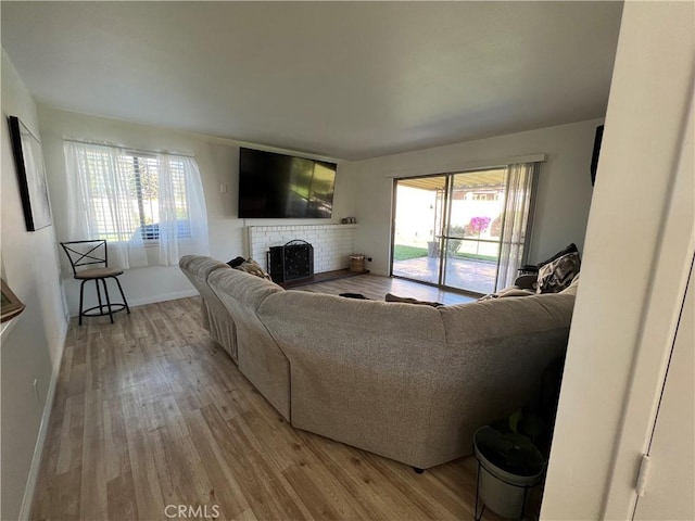 living room with a healthy amount of sunlight, a brick fireplace, baseboards, and wood finished floors