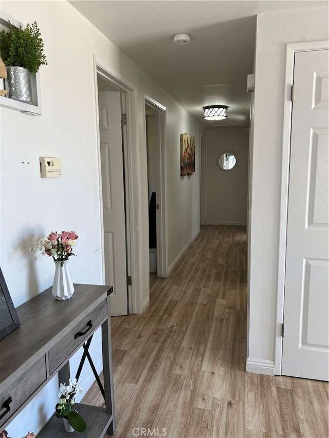 corridor featuring light wood finished floors and baseboards