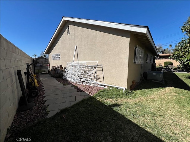 view of side of property featuring a gate, stucco siding, a yard, and fence