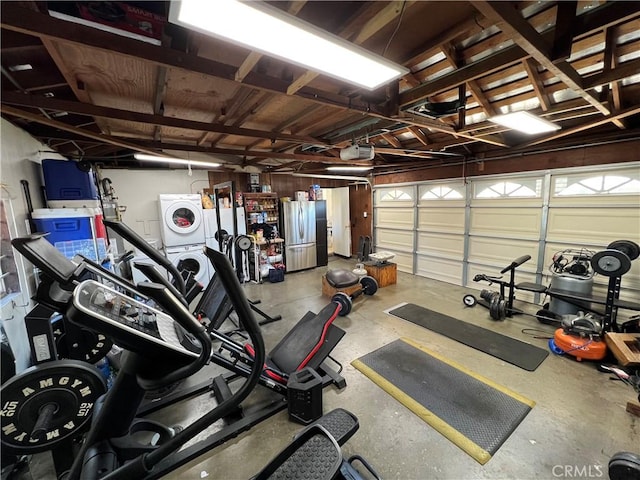 garage with a garage door opener, freestanding refrigerator, and stacked washing maching and dryer