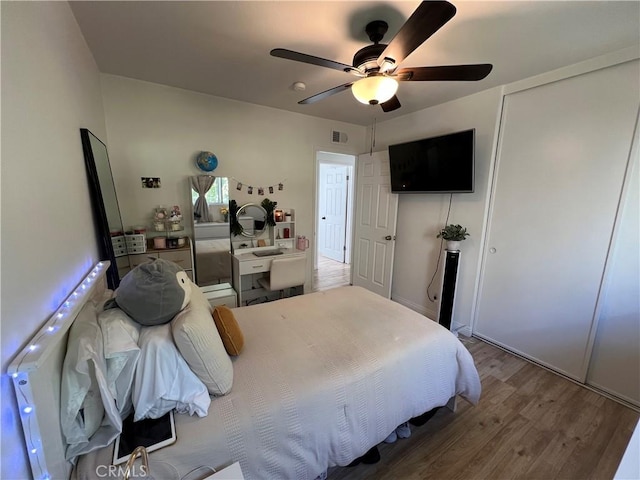 bedroom with a ceiling fan, wood finished floors, visible vents, and a closet