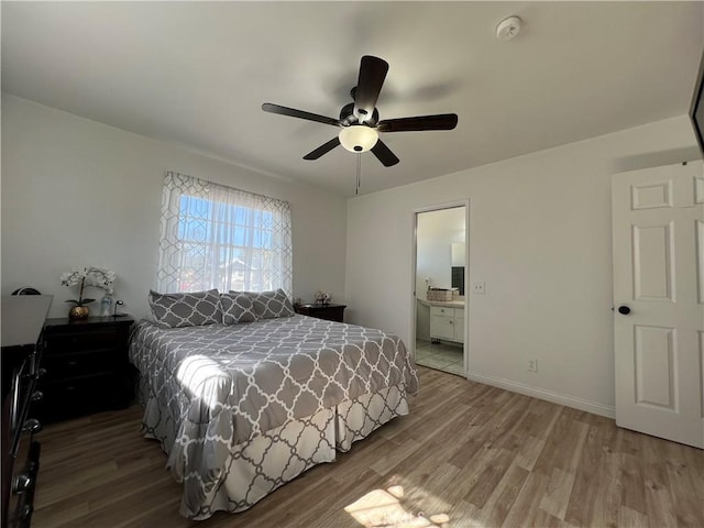 bedroom featuring ceiling fan, ensuite bath, baseboards, and wood finished floors