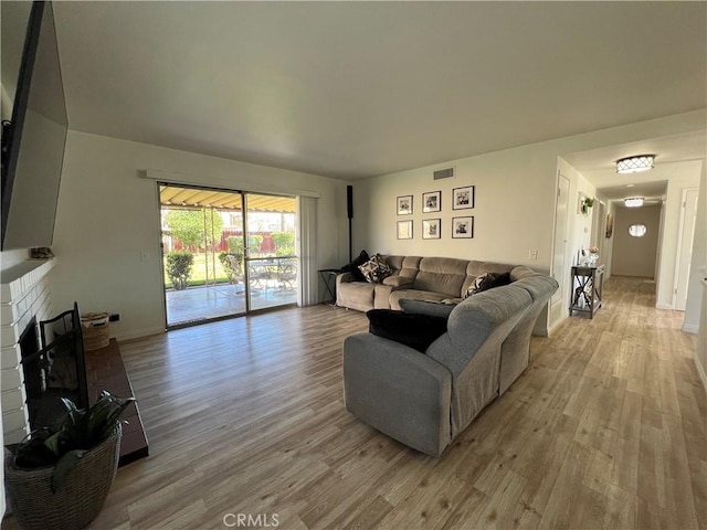 living room featuring visible vents, baseboards, a brick fireplace, and wood finished floors