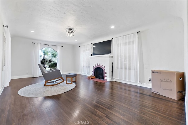 living area featuring a brick fireplace, wood finished floors, baseboards, and a textured ceiling