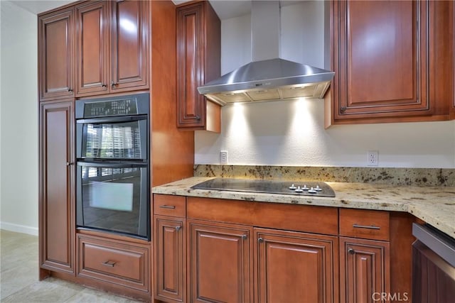 kitchen featuring black appliances, brown cabinetry, wall chimney exhaust hood, and light stone countertops