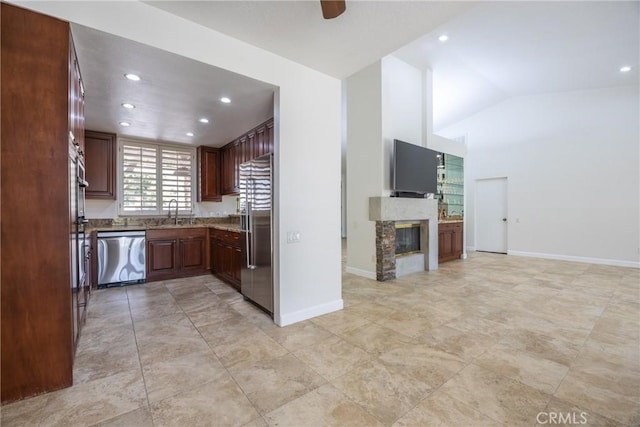 kitchen featuring open floor plan, lofted ceiling, appliances with stainless steel finishes, a glass covered fireplace, and a sink