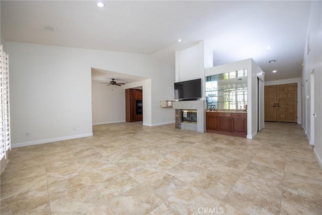 unfurnished living room with a ceiling fan, visible vents, baseboards, vaulted ceiling, and a glass covered fireplace