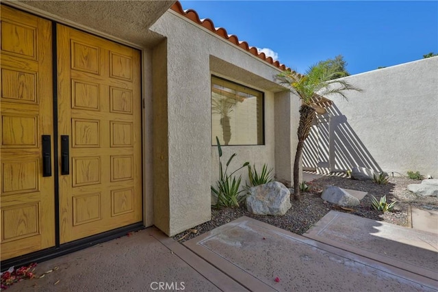 view of exterior entry with a tile roof and stucco siding