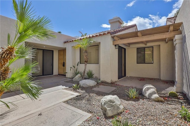 property entrance with stucco siding, a chimney, and a tile roof