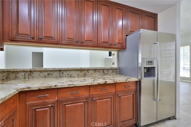 kitchen featuring light tile patterned floors, light stone countertops, stainless steel refrigerator with ice dispenser, and reddish brown cabinets