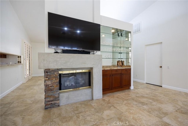 living room with a glass covered fireplace, lofted ceiling, baseboards, and visible vents