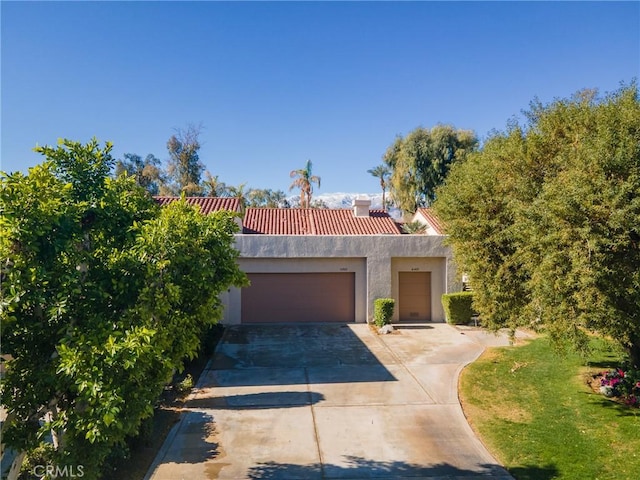 view of front of house with stucco siding, a chimney, driveway, and a tile roof