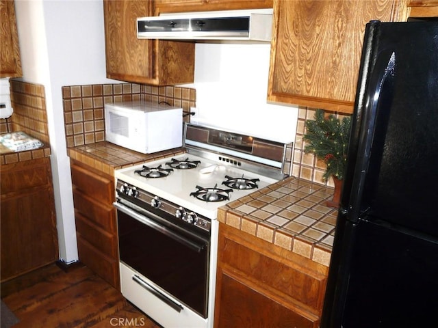 kitchen with under cabinet range hood, white appliances, backsplash, and tile countertops