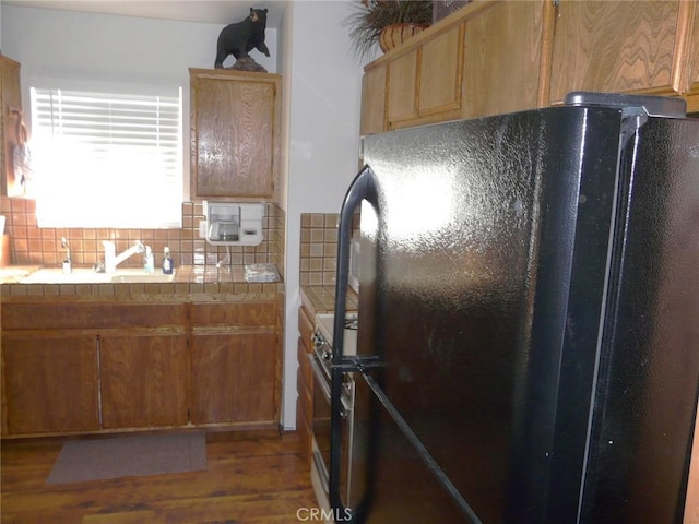 kitchen with tile countertops, wood finished floors, gas stove, freestanding refrigerator, and decorative backsplash