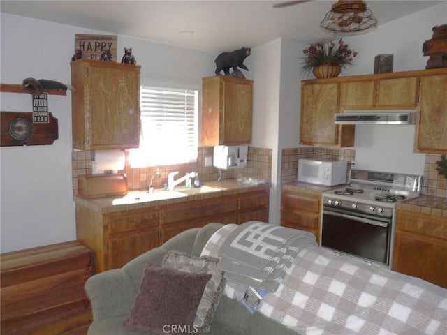 kitchen with backsplash, ventilation hood, gas range, white microwave, and tile counters