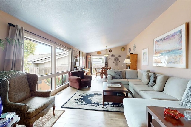 living room featuring lofted ceiling, light wood-type flooring, and a textured ceiling