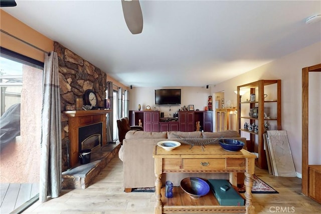 living area featuring light wood finished floors, a fireplace, and a ceiling fan