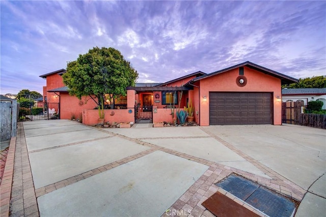 view of front of house featuring stucco siding, driveway, a gate, fence, and an attached garage