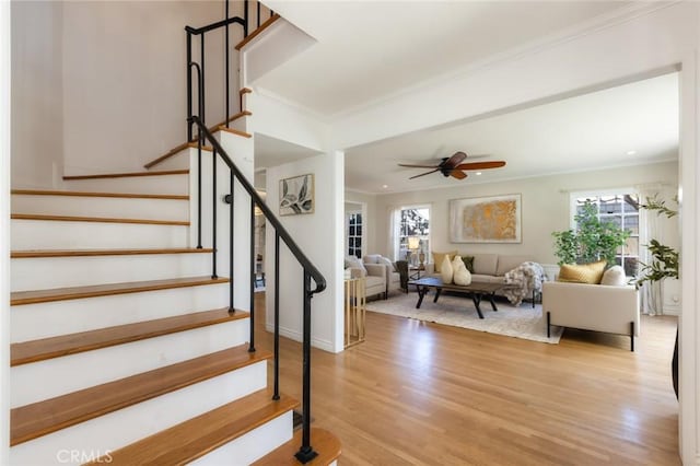 stairs featuring a ceiling fan, wood finished floors, and ornamental molding