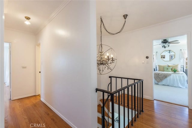 corridor with an upstairs landing, baseboards, wood finished floors, and crown molding