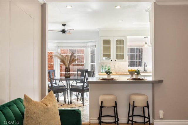 kitchen with glass insert cabinets, a breakfast bar, decorative backsplash, white cabinets, and a ceiling fan