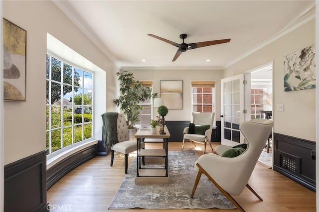 living area featuring wood finished floors, a wainscoted wall, french doors, and ornamental molding