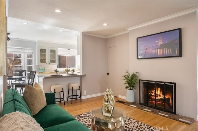 living area featuring a warm lit fireplace, recessed lighting, crown molding, light wood finished floors, and baseboards