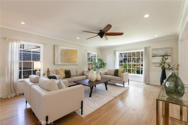 living room featuring light wood-type flooring, recessed lighting, wainscoting, crown molding, and ceiling fan