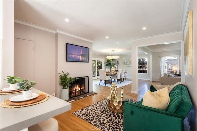 living room featuring a lit fireplace, recessed lighting, light wood-style floors, and ornamental molding