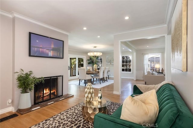 living room with light wood finished floors, crown molding, baseboards, recessed lighting, and a warm lit fireplace