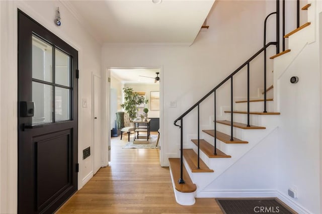 foyer featuring stairs, crown molding, light wood-style flooring, and baseboards