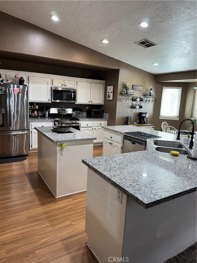 kitchen with visible vents, a sink, wood finished floors, stainless steel appliances, and a large island with sink