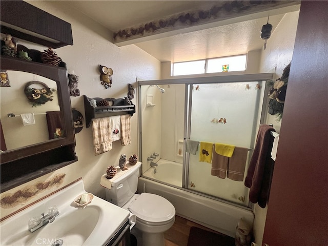 bathroom featuring vanity, toilet, a textured wall, and enclosed tub / shower combo