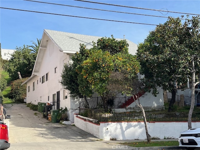 view of property exterior with stucco siding, a shingled roof, and fence